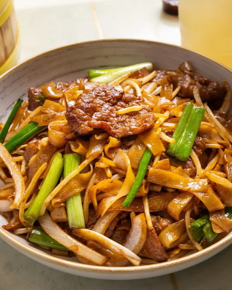 Wok-fired flat rice noodles with sliced meat, bean sprouts and spring onion in a bowl