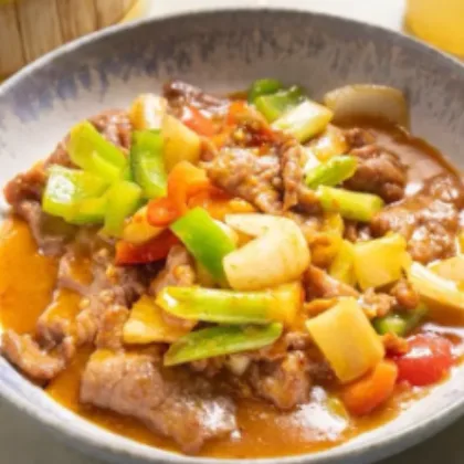 Sliced beef simmered with green peppers, onion and tomato in a light wok sauce in a ceramic bowl at Bao Express