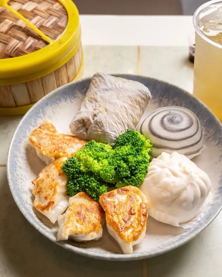Pan-fried dumplings with fresh broccoli, a swirled steamed bun and a sticky rice wrap on a stone plate