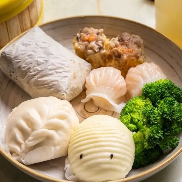 Dim sum plate with a sticky rice wrap, pork siu mai, shrimp har gow, steamed bao and broccoli