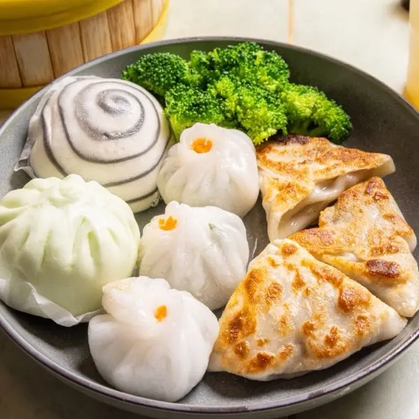 Dim sum plate with a swirled bun, steamed bao, shrimp har gow, pot stickers and broccoli