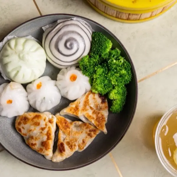 Overhead dim sum plate with steamed buns, shrimp har gow, pot stickers and broccoli beside jasmine tea