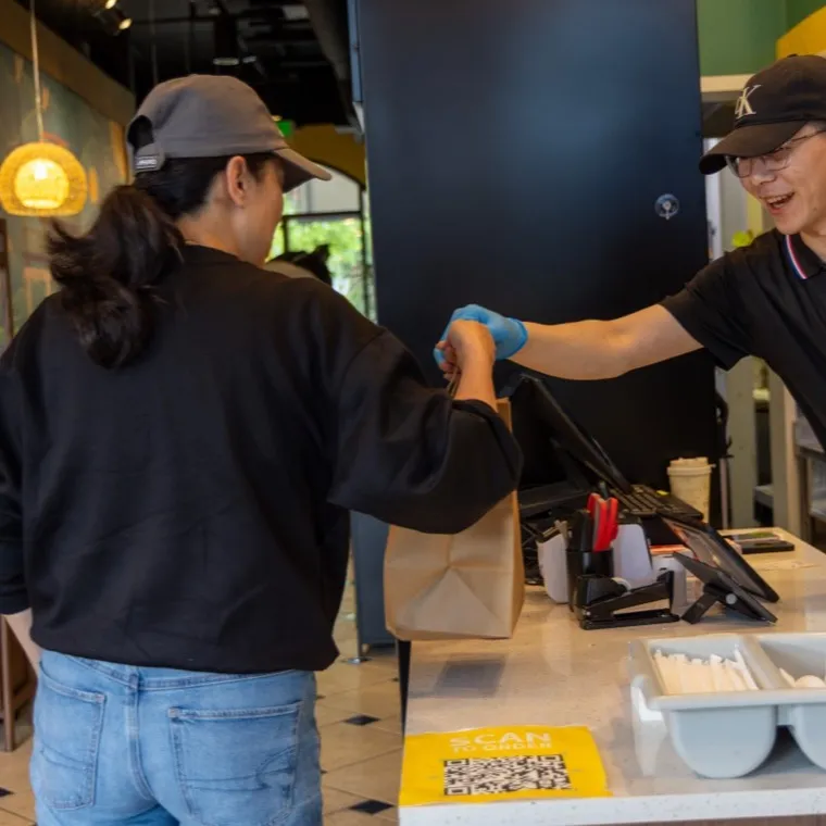 A Bao Express team member handing a takeout order across the pickup counter to a customer