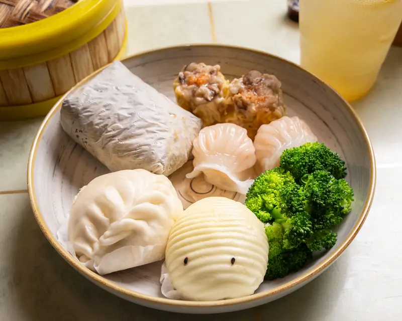 A plated selection of har gow, shumai and bao served with fresh broccoli at Bao Express in San Mateo